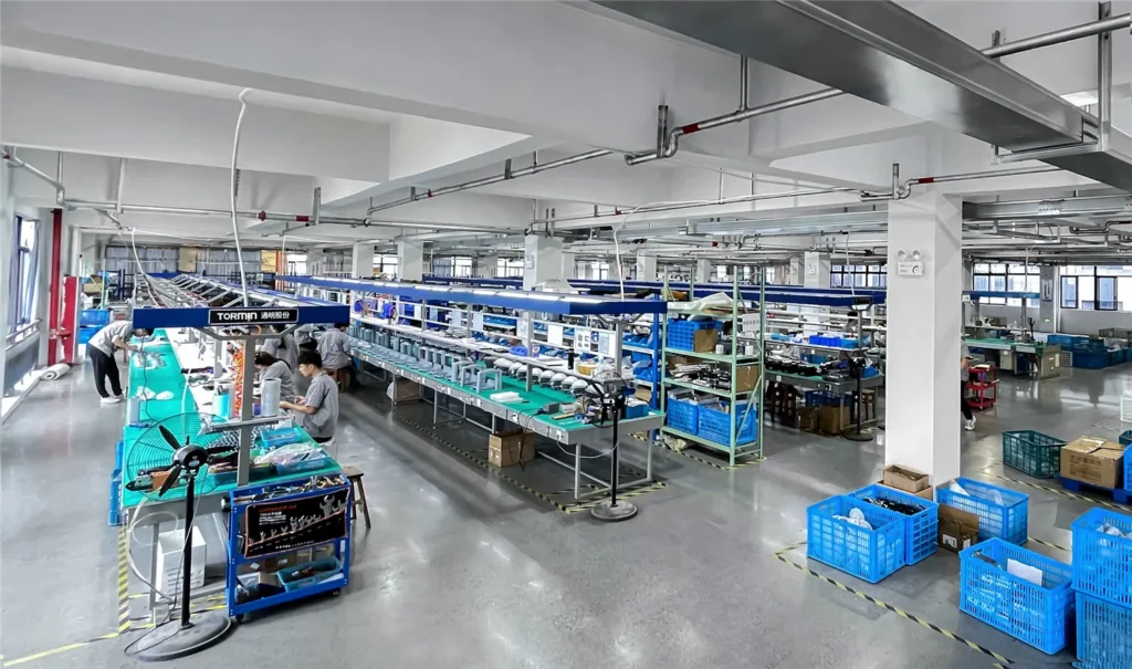 Technicians assembling lighting products at workbenches in the TORMIN workshop.